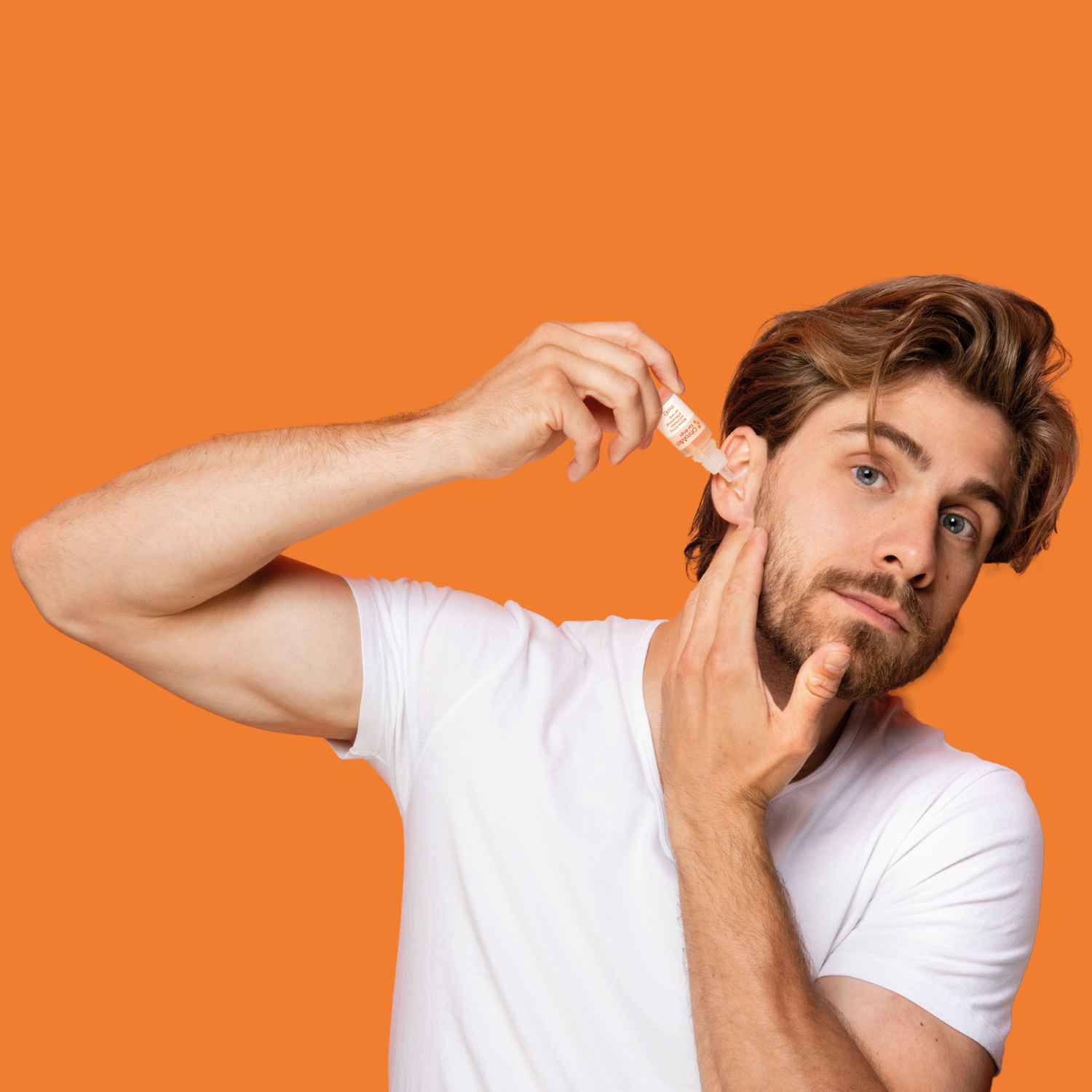 A man in a white shirt applies OhroMel ear drops into his ear, set against an orange background with a subtle honeycomb pattern.